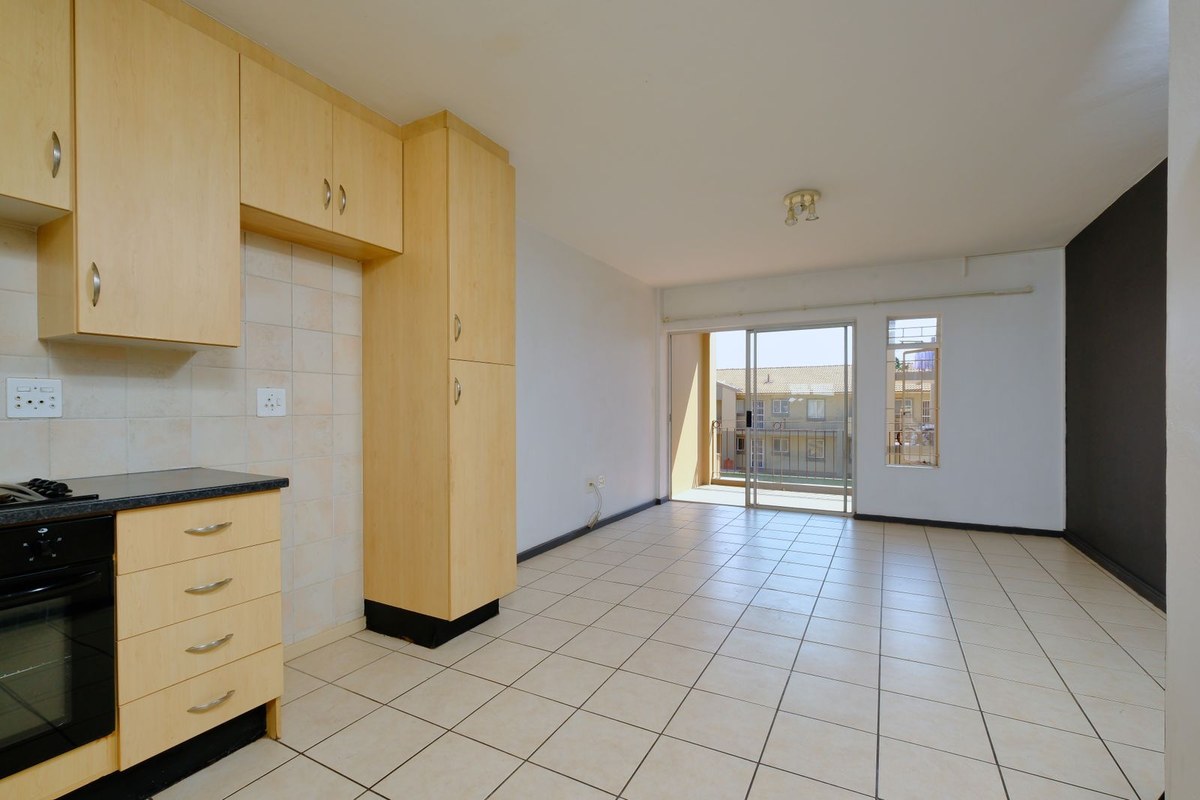 Vacant apartment with light-wood kitchenette, tiled floor, and sliding door to balcony